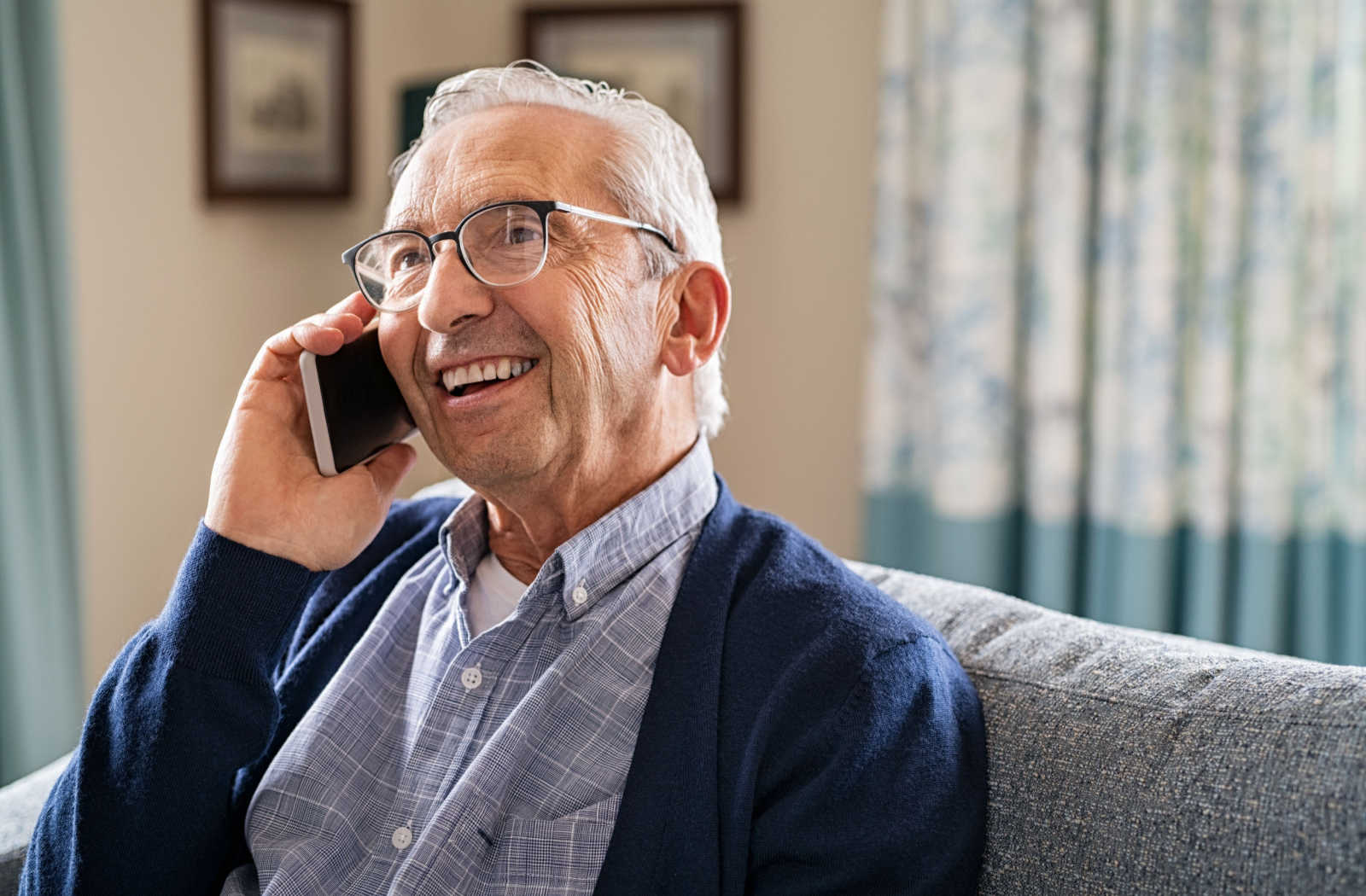 A senior man with grey hair and glasses smiling while talking on a smartphone.