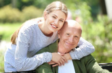 A senior man and his daughter in a park, smiling and looking directly at the camera