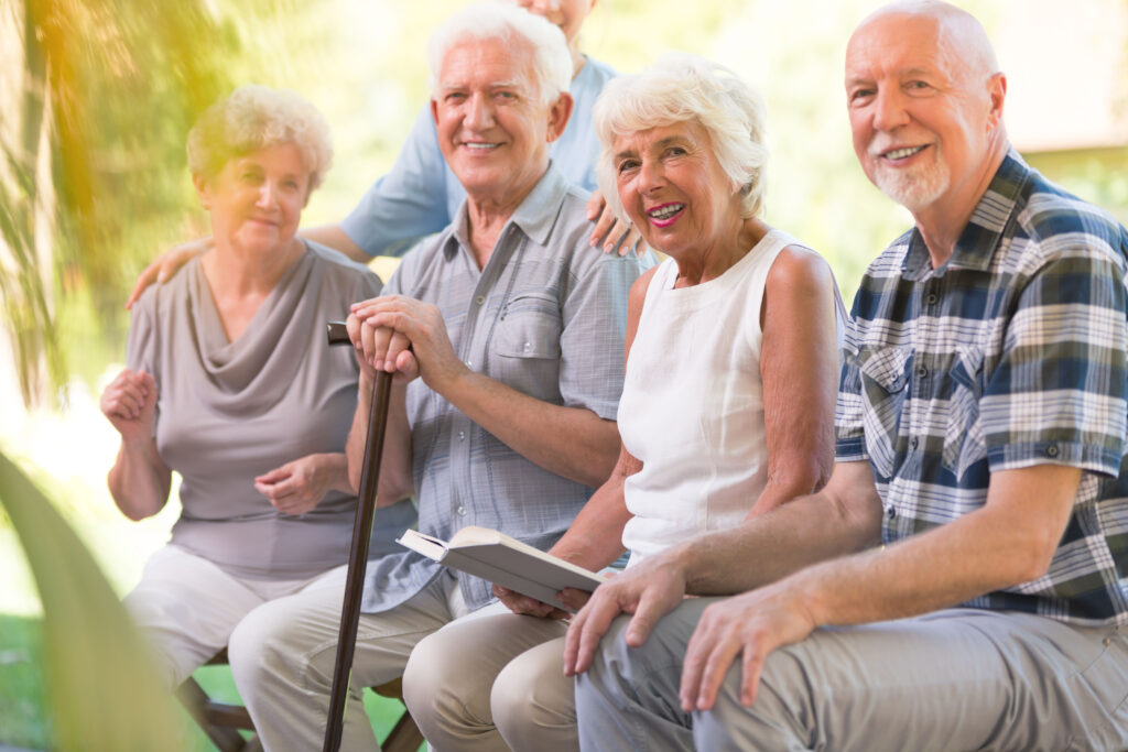 A group of smiling seniors sitting outside with a nurse and looking directly at the camera