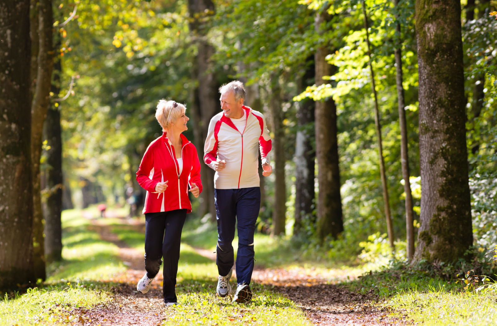 An older adult couple jogging together along a park trail.
