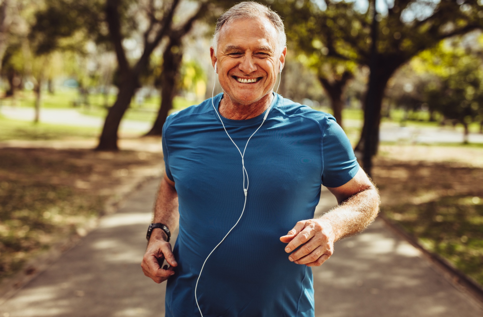 An older adult man jogging outside while listening to music.