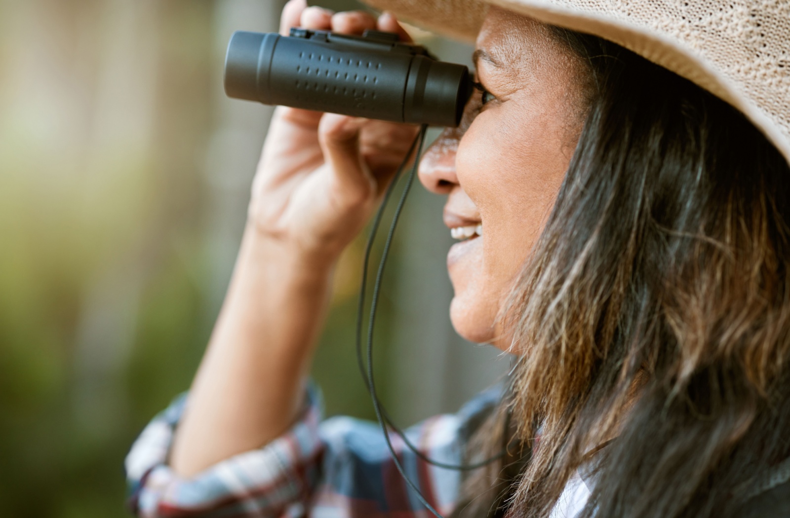 Older woman birdwatching outdoors with binoculars.