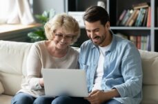 An older adult sits with their child and browses assisted living communities on a laptop.